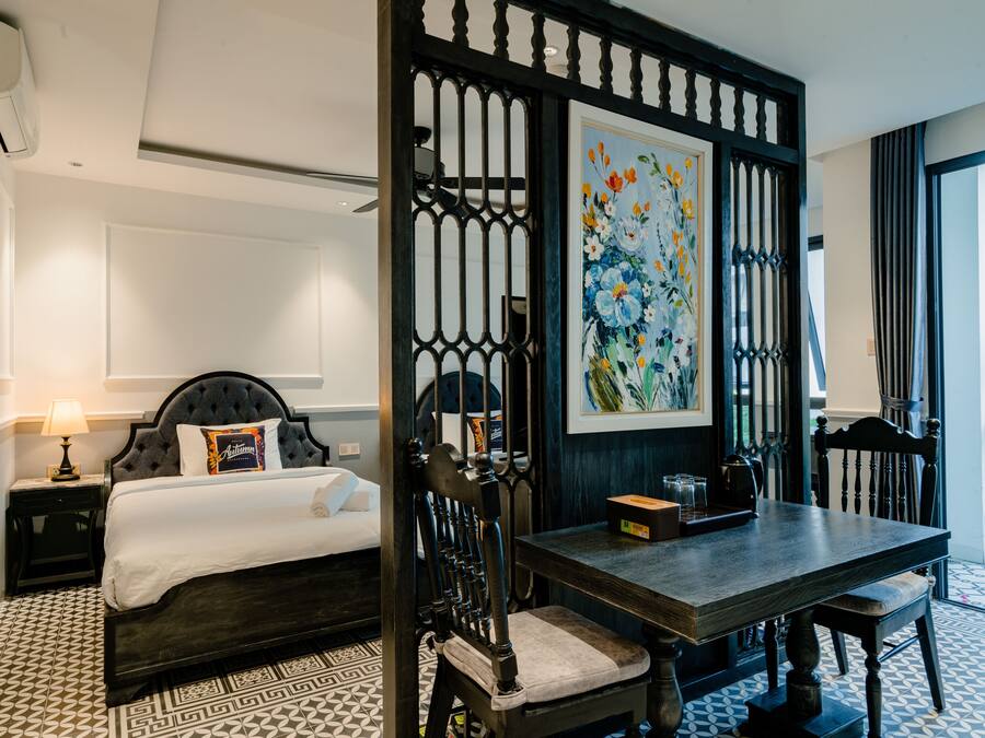 A hotel room with a bed, a desk, a chair, a decorative screen, and a painting.