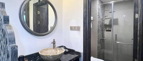 A bathroom with a round mirror, a vessel sink, a toilet, and a glass-enclosed shower.