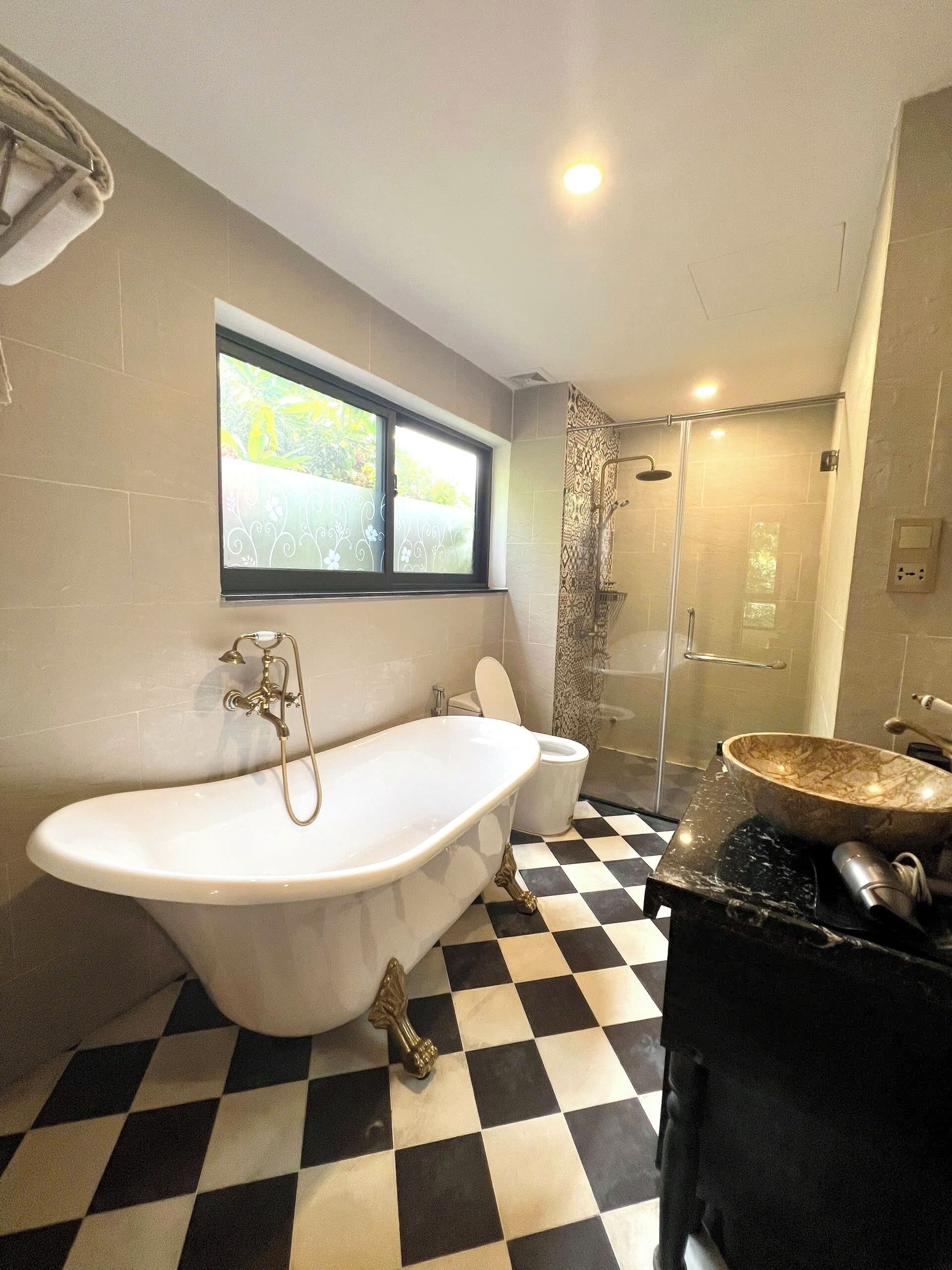A bathroom with a freestanding bathtub, a toilet, a shower enclosure, and a checkered floor.