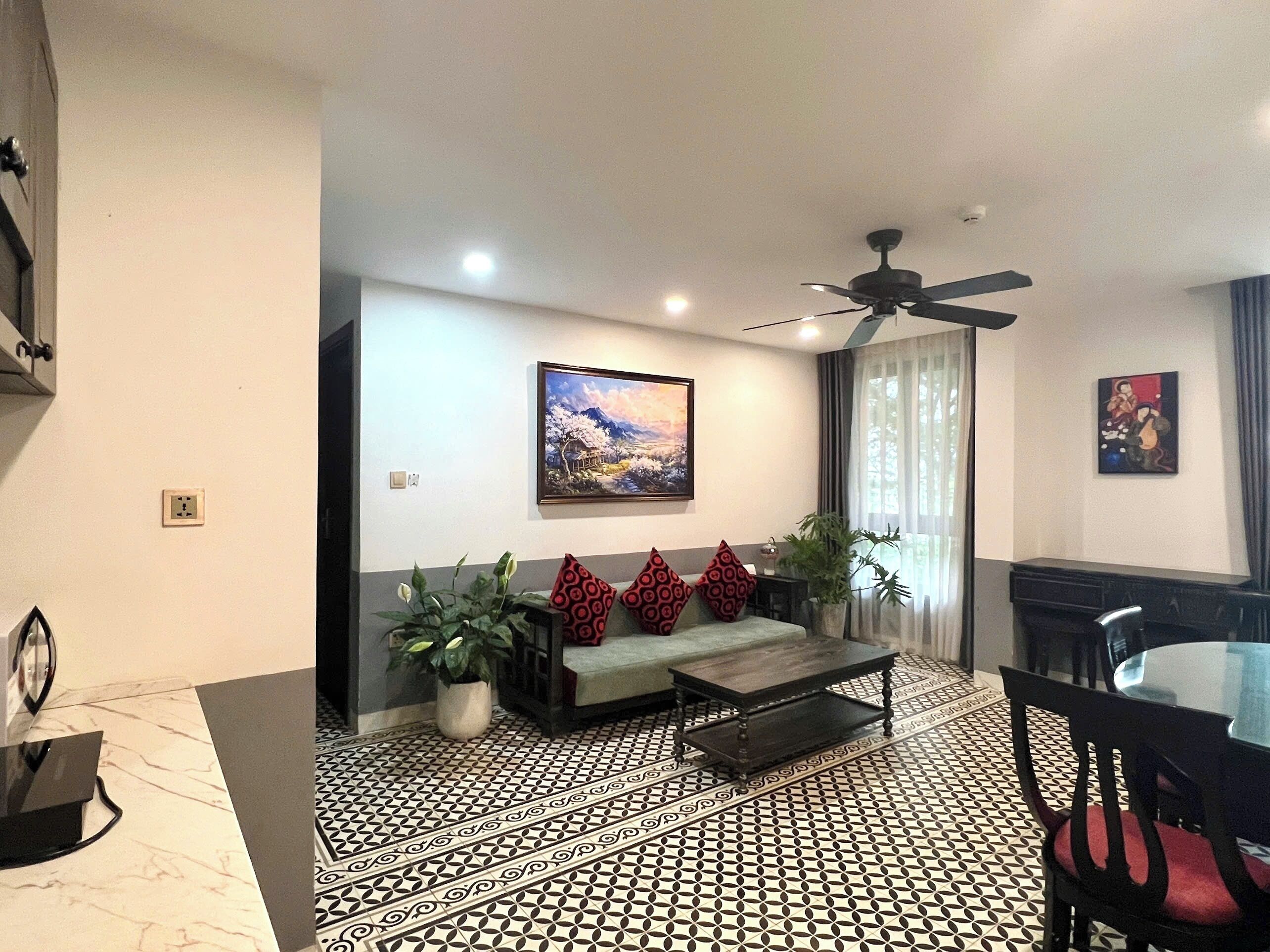 A modern living room with a sofa, a coffee table, a dining table with chairs, a ceiling fan, and a painting on the wall.