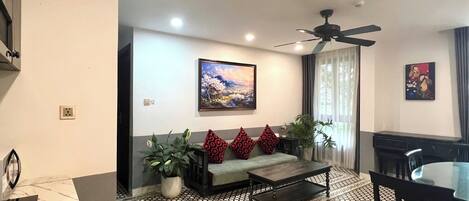 A modern living room with a sofa, a coffee table, a dining table with chairs, a ceiling fan, and a painting on the wall.