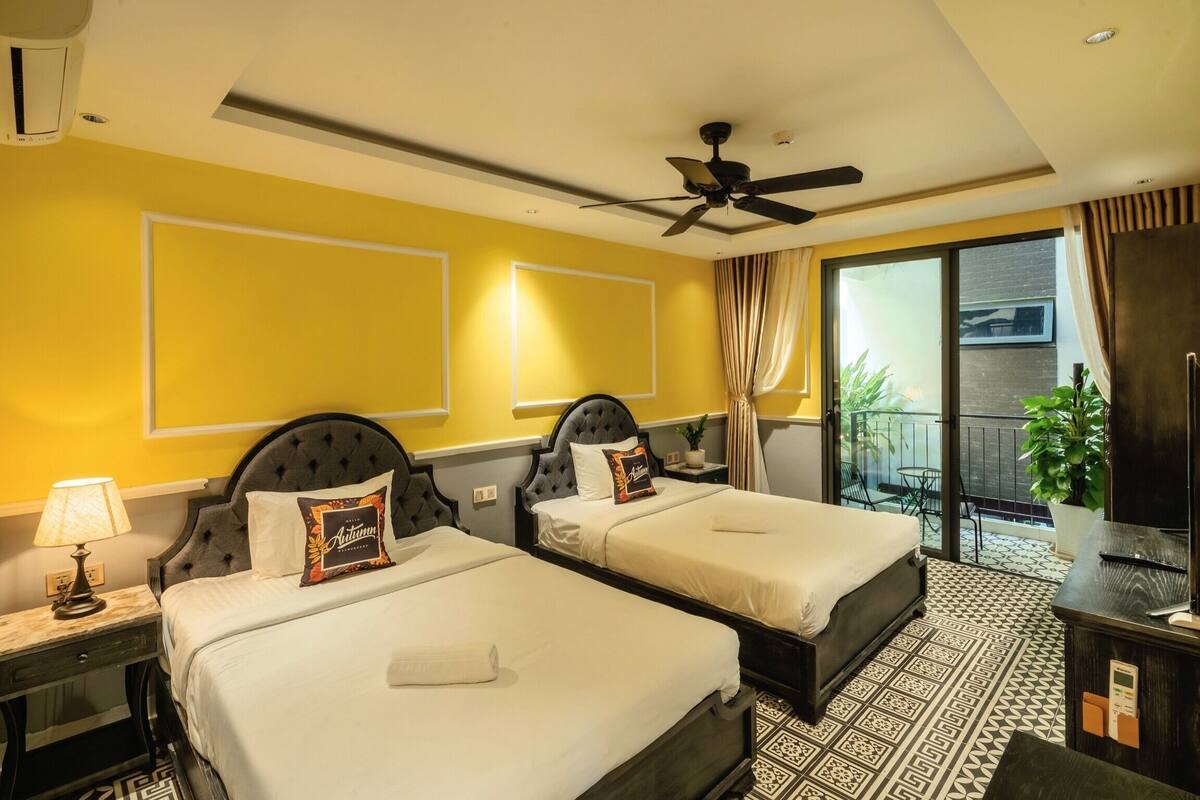 A hotel room with two beds, a ceiling fan, a balcony with a view, and a desk with a lamp.