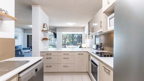 Ett modernt kök med en central köksö, inbyggda vitvaror och utsikt mot utomhusmiljön.