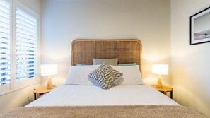 A bedroom with a wicker headboard, white bedding, two bedside lamps, and a framed picture on the wall. - Bay Parklands, 29 2 Gowrie Avenue - views, air conditioning, Wi-Fi, Pool, tennis court and spa (Nelson Bay)