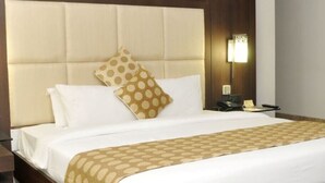 A hotel room with a large bed, a nightstand, a lamp, and a wooden side table.