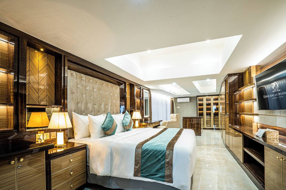 A modern hotel room with a large bed, a vanity with a mirror, a TV, and a walk-in closet.