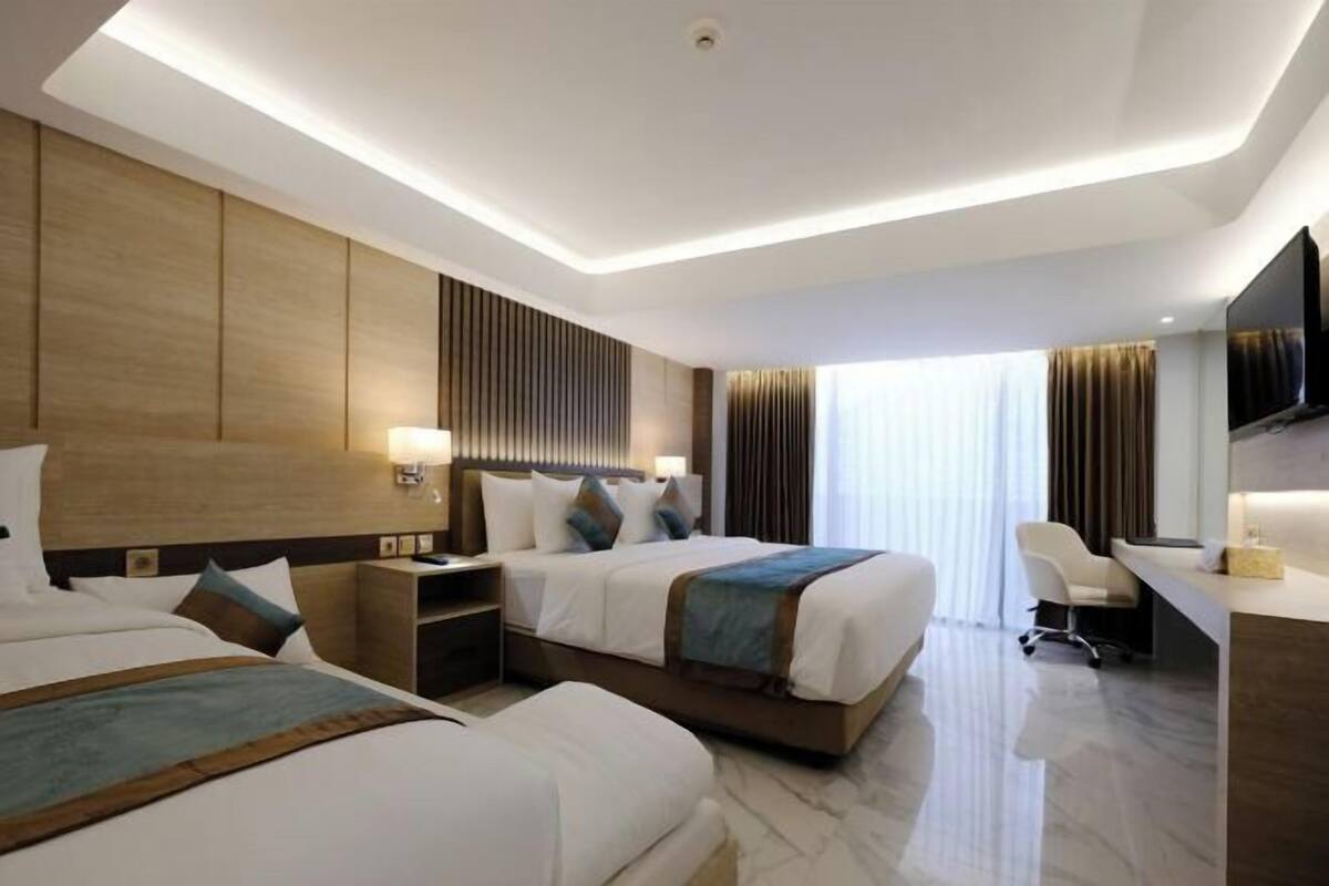 Hotelkamer met twee bedden, een bureau, een stoel, een televisie en een groot raam met gordijnen.