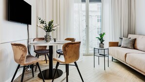 Una sala de estar moderna con una mesa de comedor redonda, sillas acolchadas, un sofá, un televisor montado en la pared y vistas a través de un ventanal.