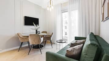 Una sala moderna con un sofá verde, una mesa de comedor con sillas, un televisor de pantalla plana y una pequeña mesita auxiliar.
