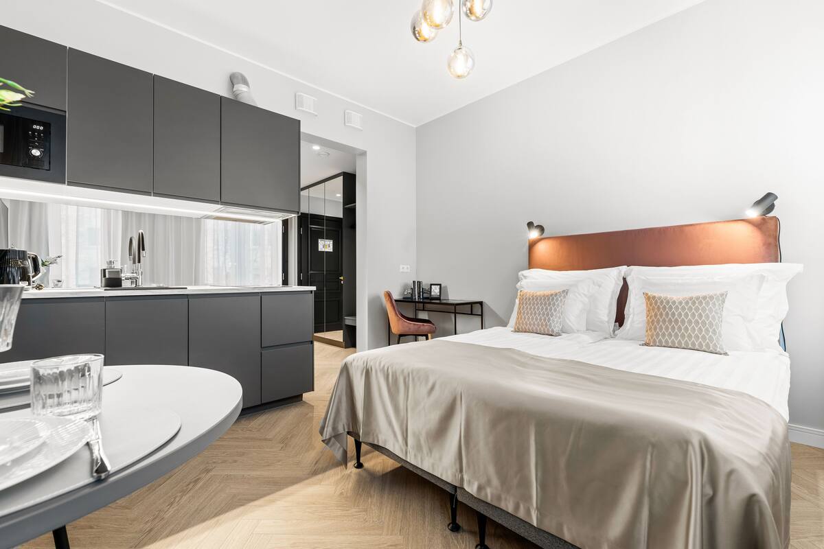 Una habitación de hotel moderna con cocina americana, una mesa de comedor y una cama con cabecera.