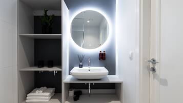 A modern bathroom with a white sink, a round mirror with underglow lighting, and shelves with toiletries.