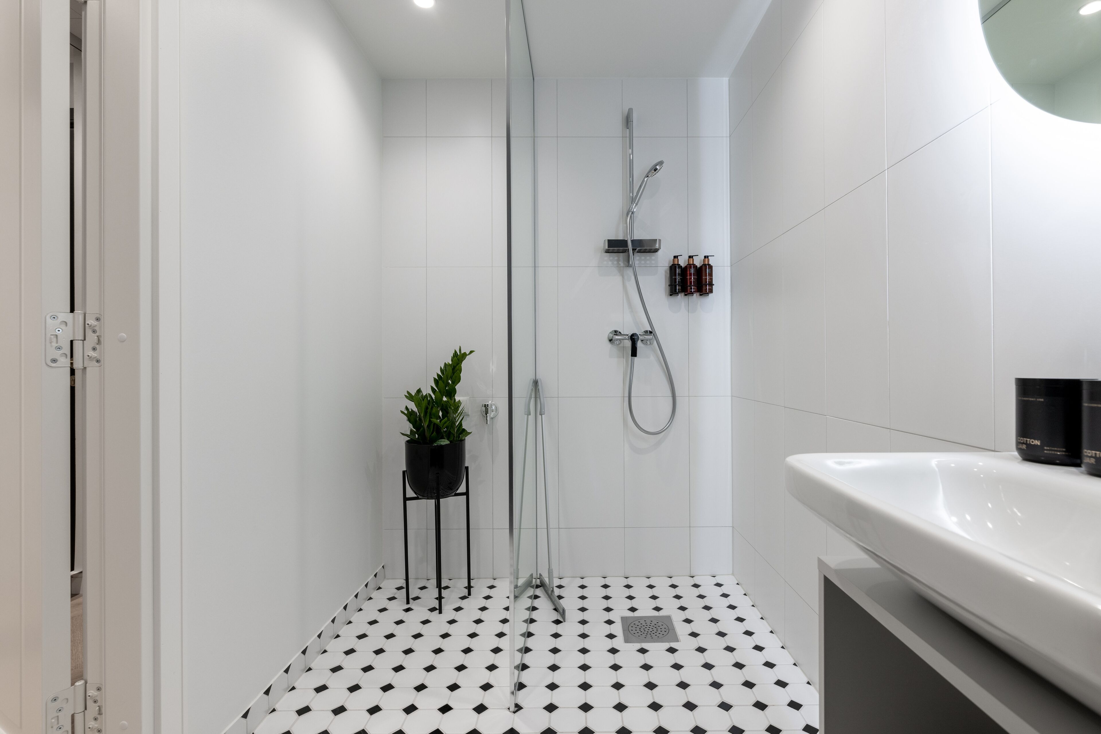 A modern bathroom with a black and white tiled floor, a white sink, and a glass-enclosed shower area.
