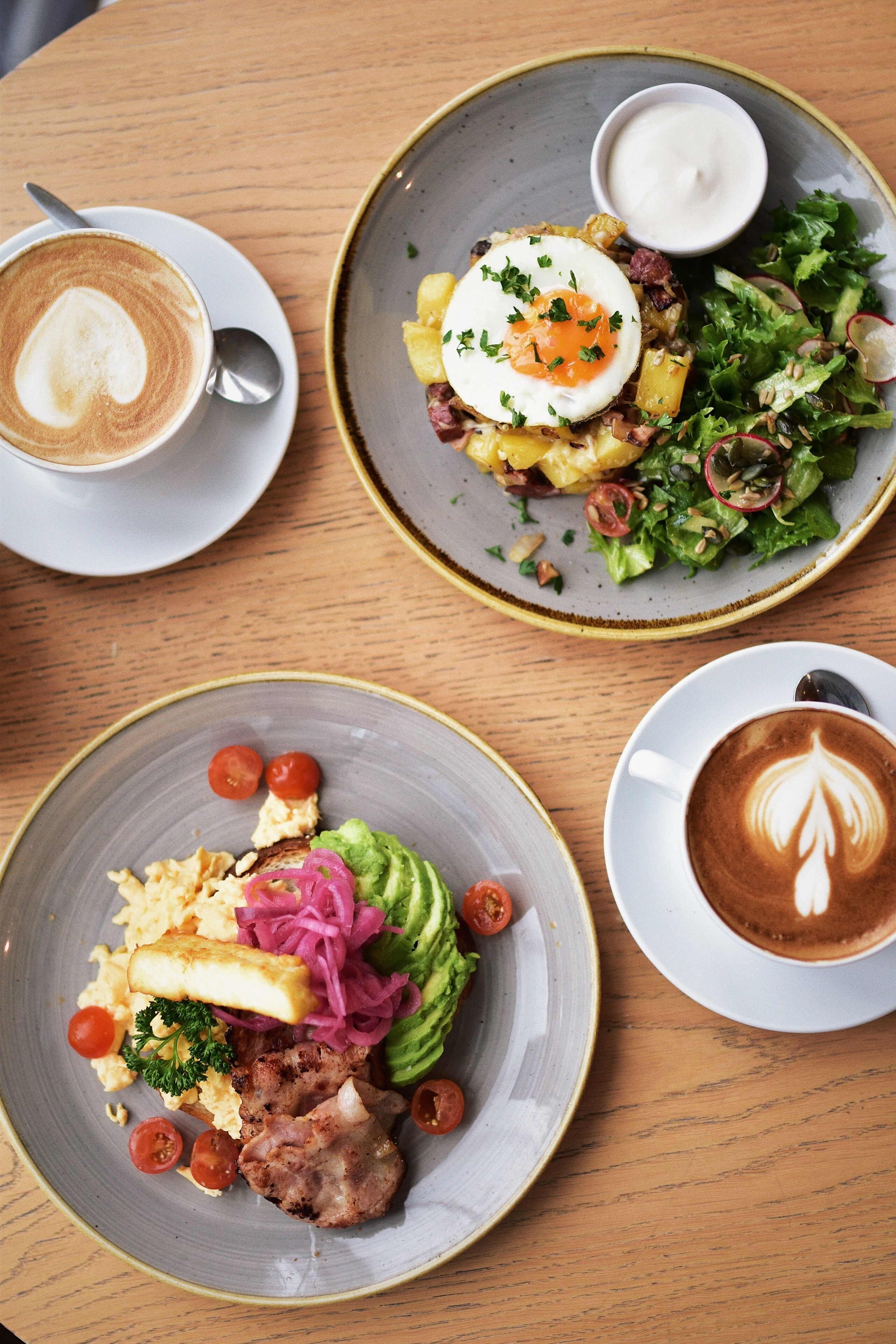 A table with three plates of food and two cups of coffee.