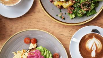 A table with three plates of food and two cups of coffee.