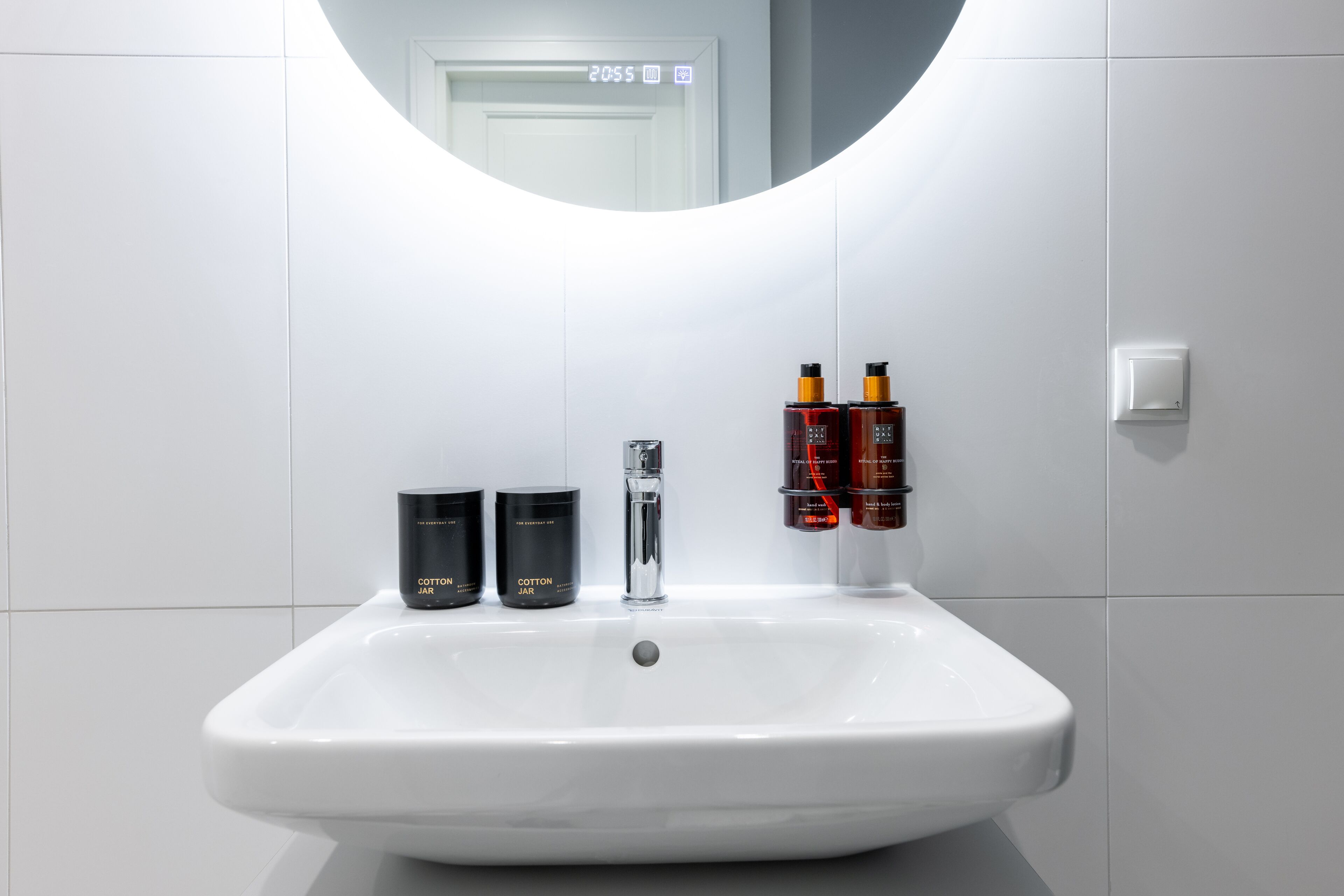 A white bathroom sink with a mirror above it, a faucet, and two black cotton jar containers.