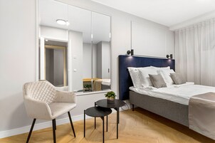 Una habitación de hotel moderna con una cama, una silla, una mesita y un espejo.