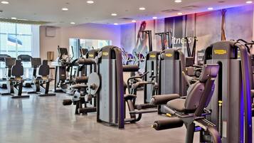 A gym with various exercise machines, including weight benches and cardio equipment, arranged in rows.