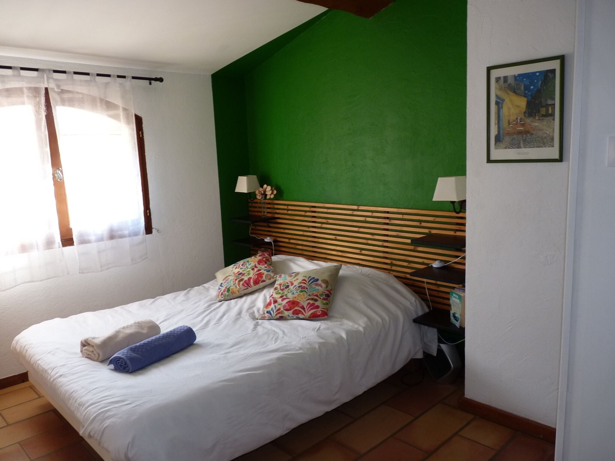 Ein Schlafzimmer mit Bett, Kissen, einem Nachttisch, einer Lampe und einem Bild an der Wand.