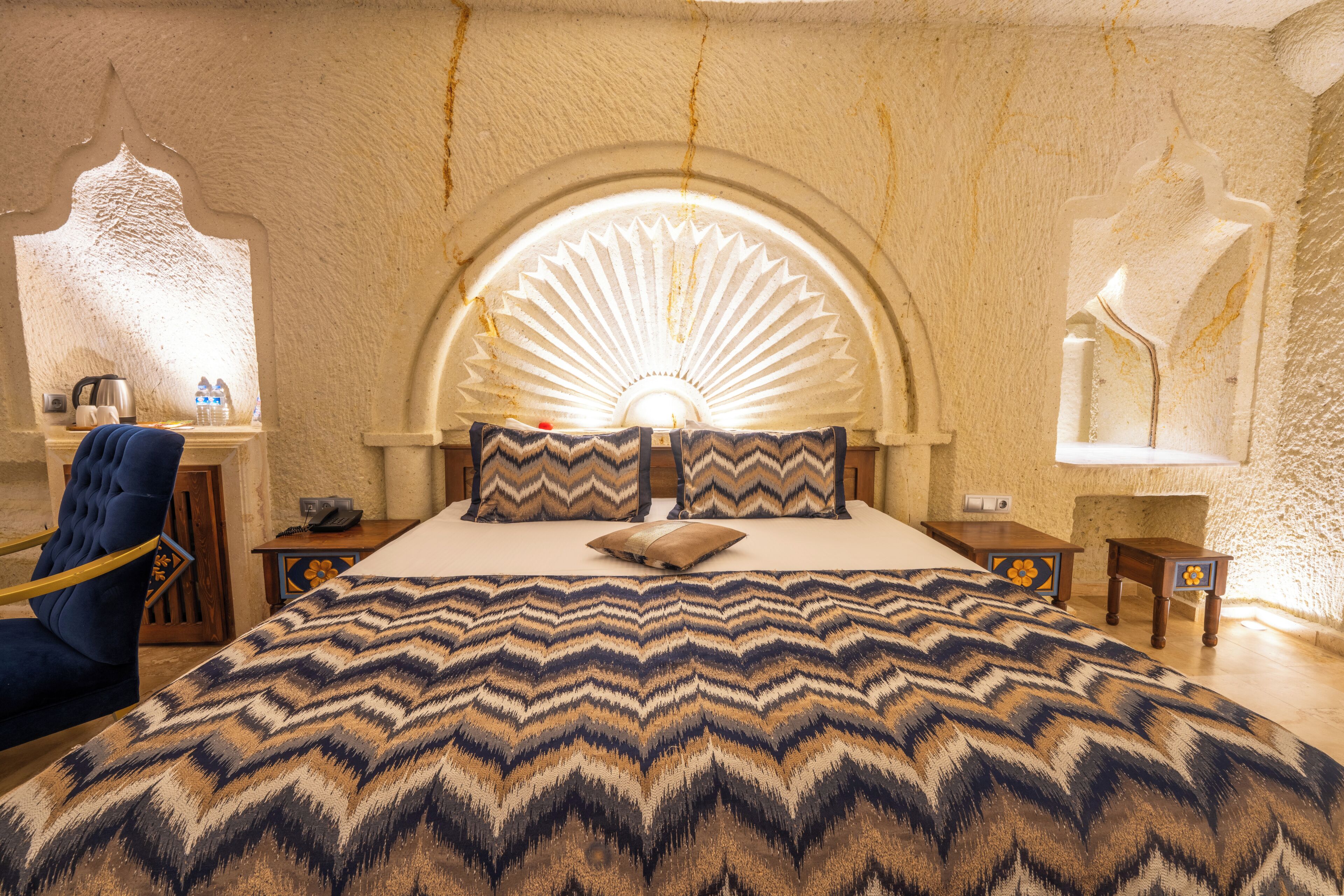 A bedroom with a large bed, a blue chair, a nightstand, and a wall-mounted lamp.