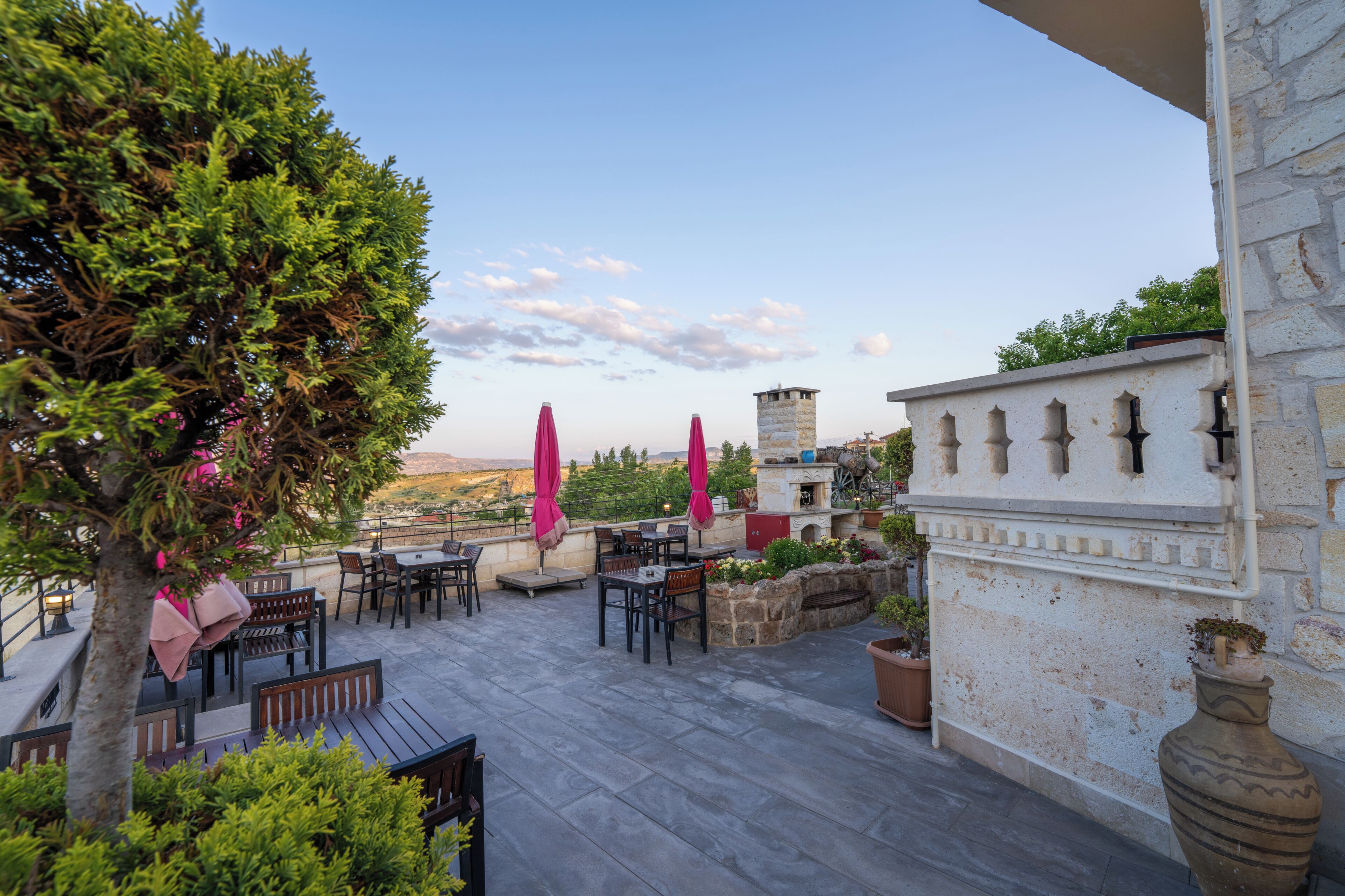 Un patio exterior con mesas y sillas, un muro de piedra y vistas al paisaje.