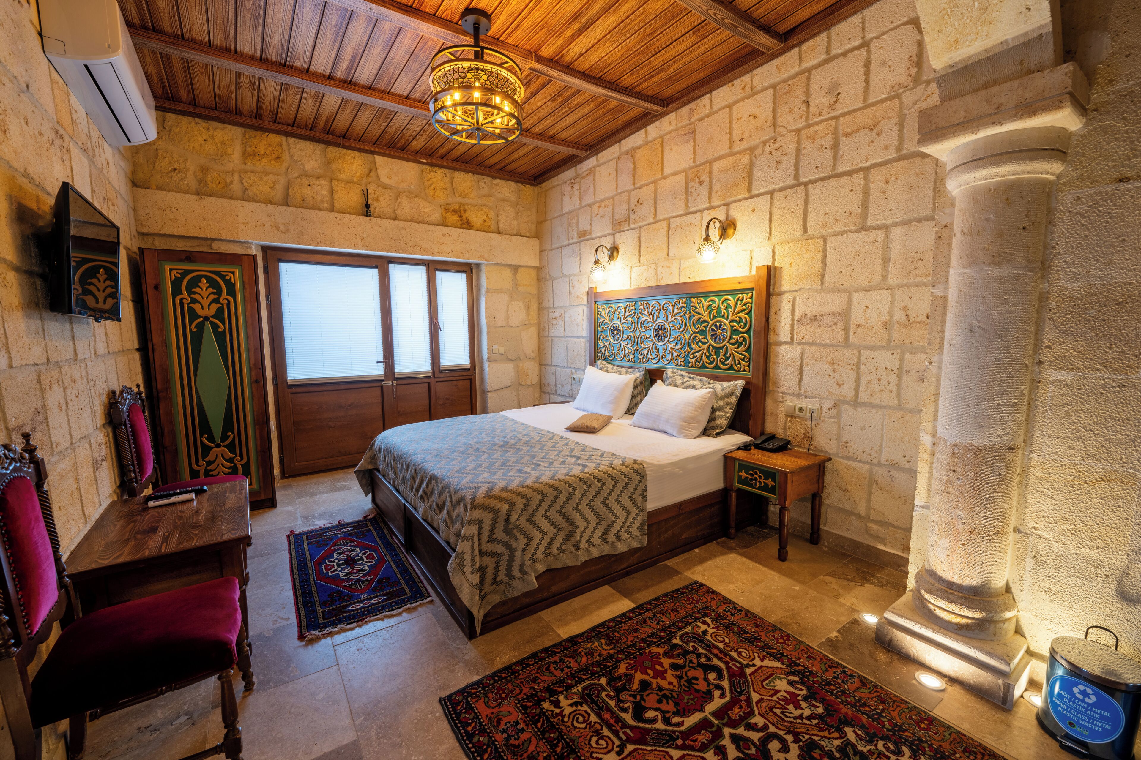 Un dormitorio con una cama, muebles de madera, una pared de piedra y una lámpara decorativa en el techo.
