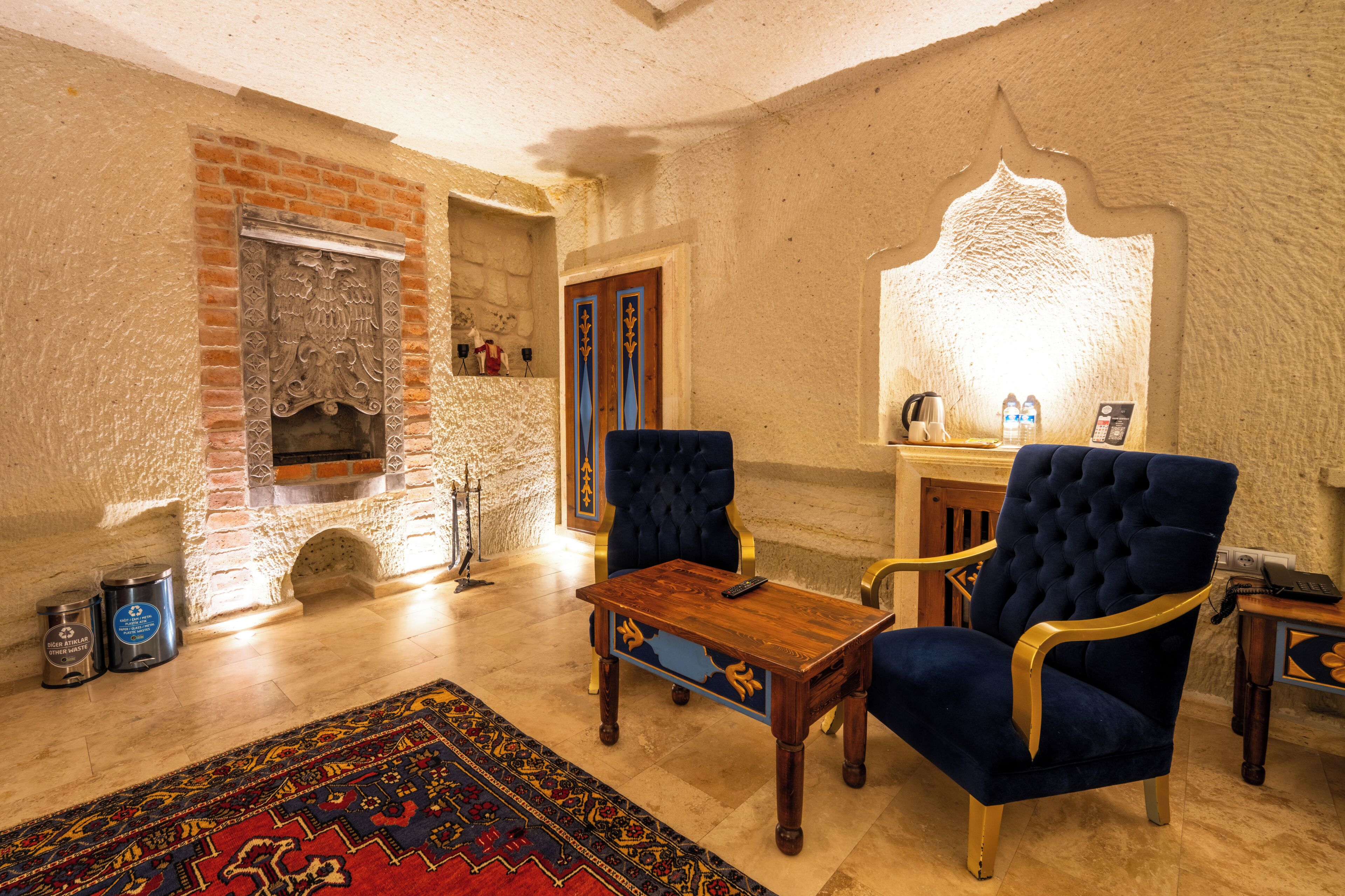 Una habitación con chimenea, dos sillones azules, una mesa de centro de madera y una alfombra estampada.