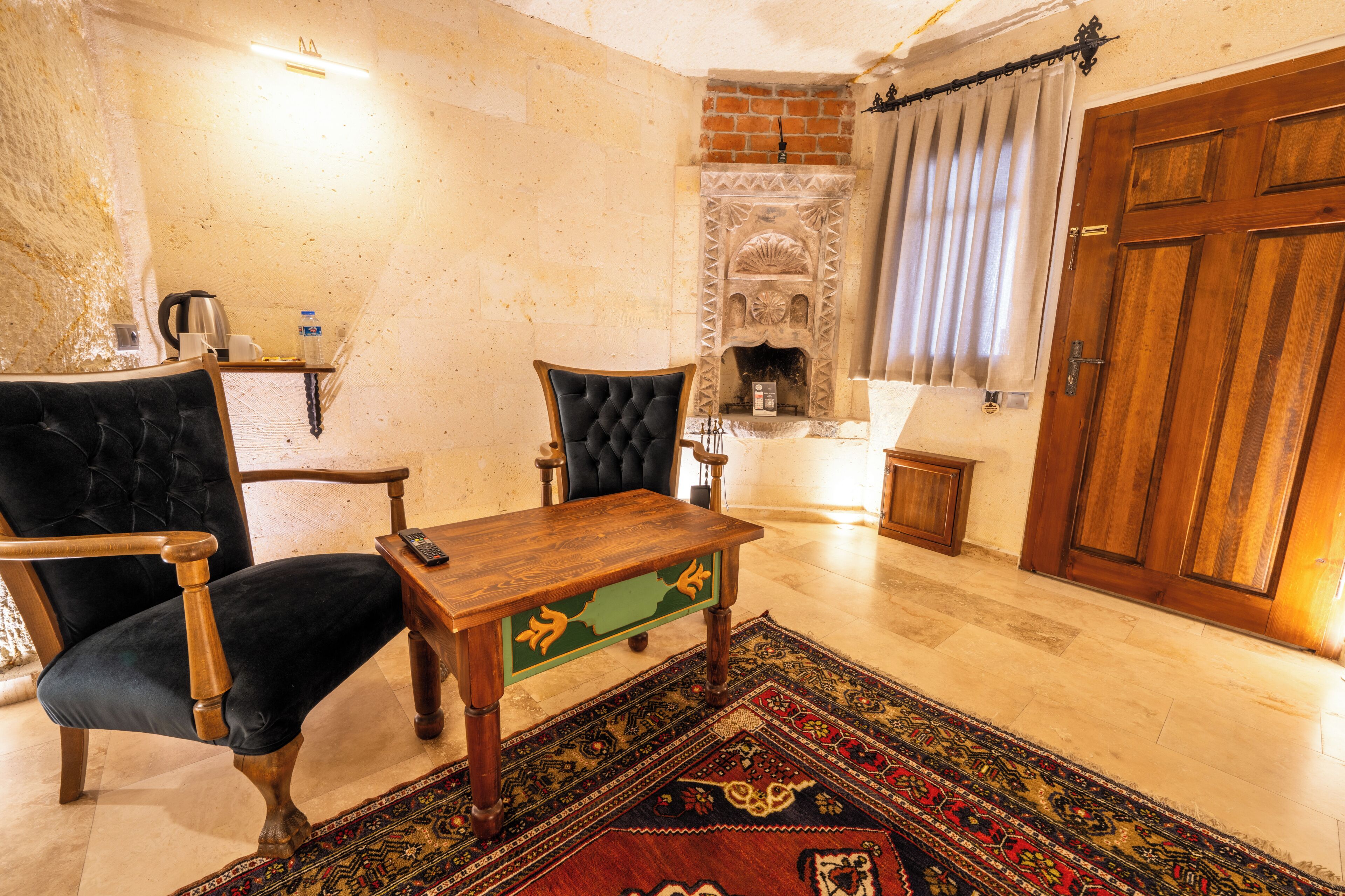Una sala de estar con chimenea, una mesa de madera, una silla negra y un tapete estampado.