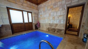 Una piscina interior con paredes de piedra, una puerta de madera y un baño visible.