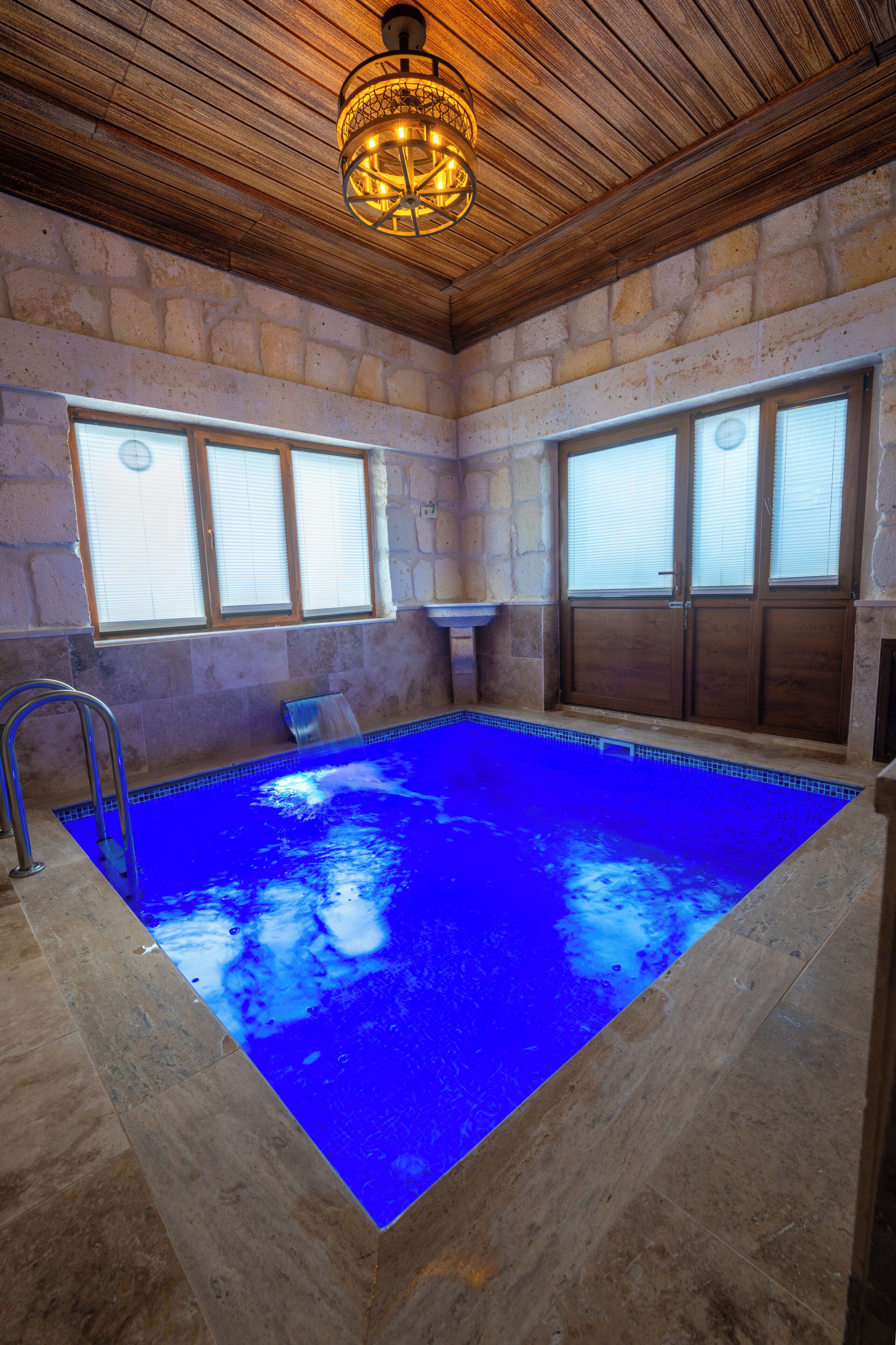 An indoor swimming pool with stone walls, wooden ceiling, and a metal ladder.