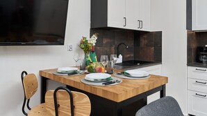A modern kitchen with a wooden dining table set for four, a flat-screen TV mounted above, and white cabinetry. - Modern Studio on Jagodno | Balcony and Parking (Wrocław)