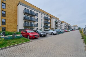 Une rangée d’immeubles d’appartements modernes dotés de balcons, une allée pavée et des voitures garées.