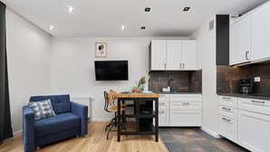 A modern kitchen with white cabinets, a wooden dining table, and a blue sofa. - Modern Studio on Jagodno | Balcony and Parking (Wrocław)
