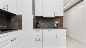 A modern kitchen with white cabinetry, a dark countertop, and a coffee maker. - Modern Studio on Jagodno | Balcony and Parking (Wrocław)