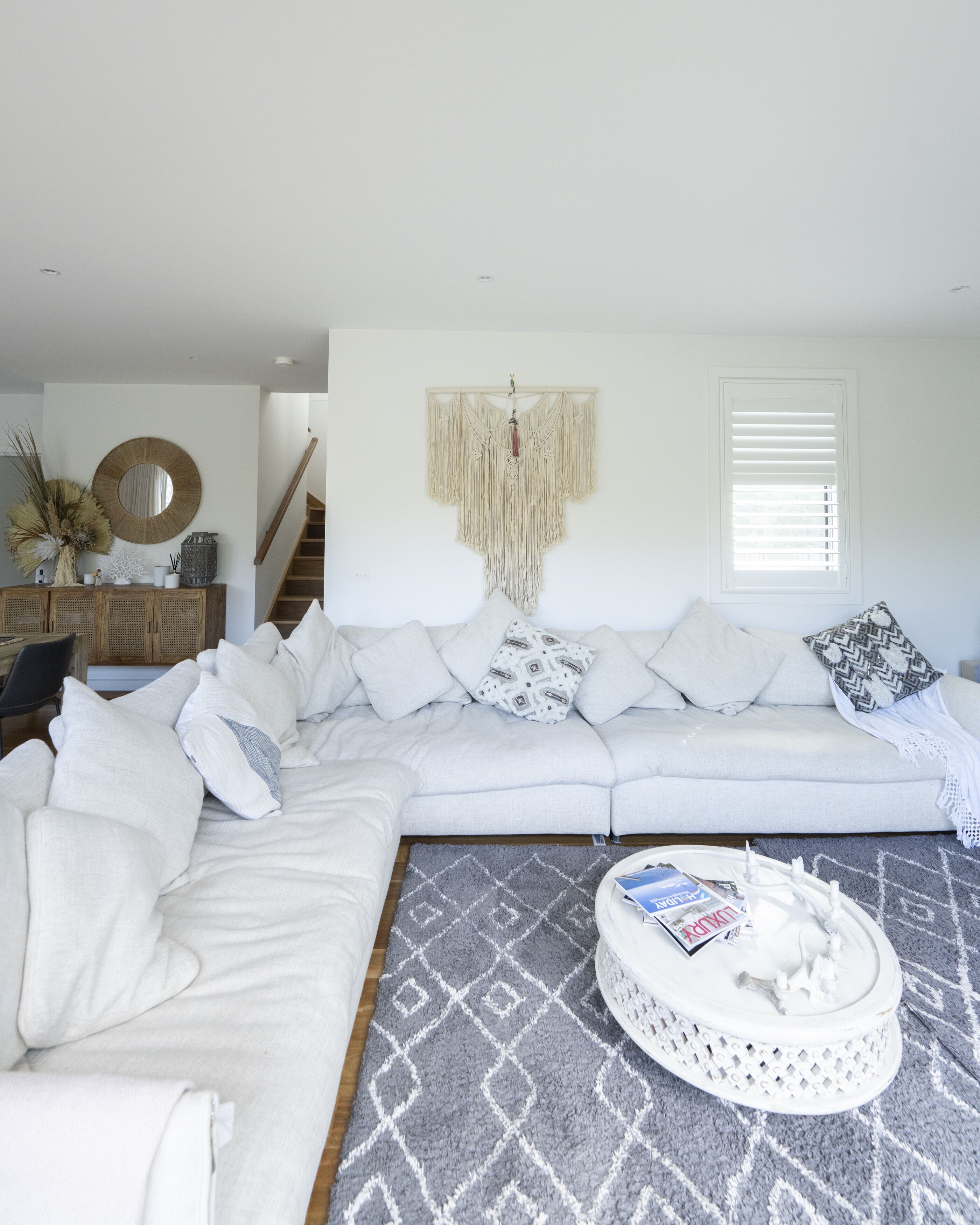 A modern living room with a white sectional sofa, a patterned rug, and a macrame wall hanging.