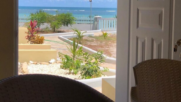 A view from a room with a door leading to a balcony overlooking a beach with palm trees and a clear sky. - Punta Rucia Cristal Beach (Villa Isabela)
