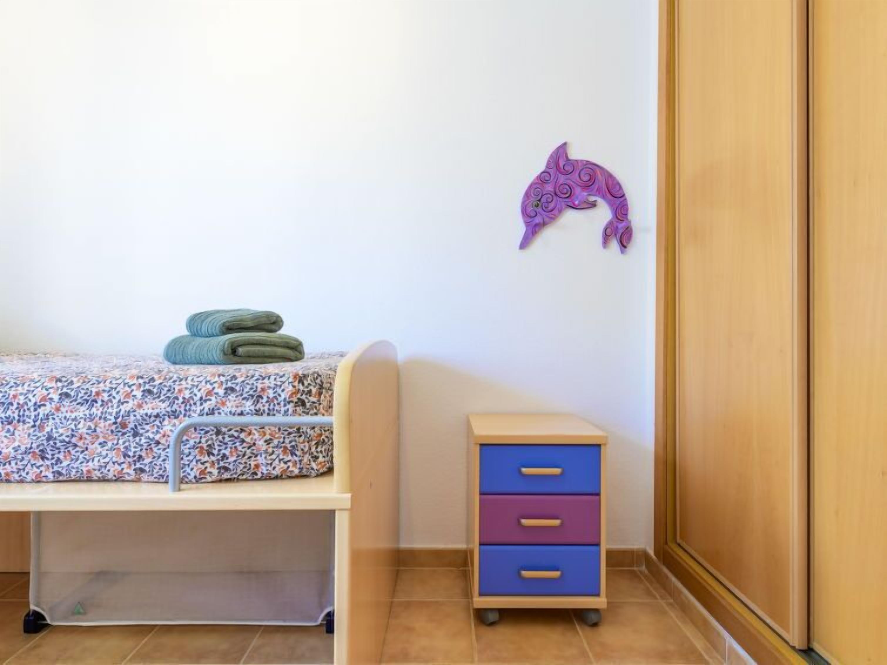 Un dormitorio infantil con una cama, un pequeño aparador y una decoración en la pared.