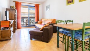 Een gezellige woonkamer met een bank, een houten tafel en stoelen. Er is een balkon met oranje gordijnen en uitzicht op gebouwen.