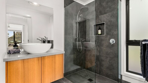 A modern bathroom with a large white sink, a glass-enclosed shower, and a wooden vanity.
