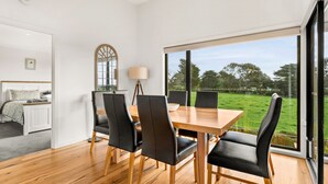 A dining area with a wooden table and black chairs, a lamp, and a view of a green field through large windows. - Castlebay - Lovely 4 bedroom home (Wimbledon Heights)