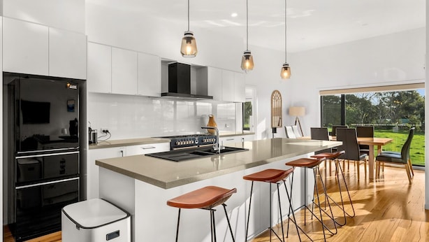 A modern kitchen with a central island, bar stools, and a dining area with a view of the outdoors. - Castlebay - Lovely 4 bedroom home (Wimbledon Heights)