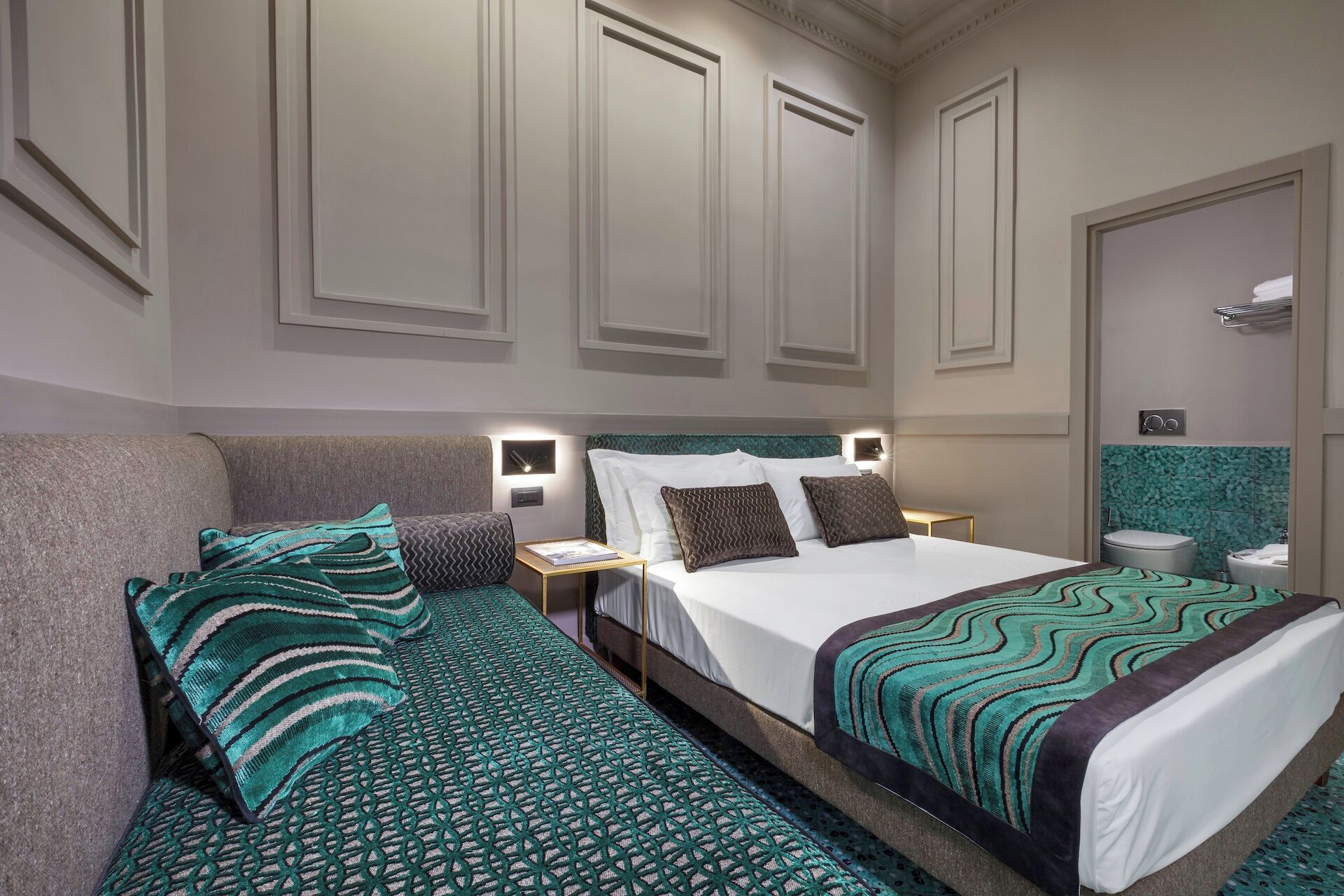 A hotel room with a bed, a nightstand, a sofa, and a bathroom.