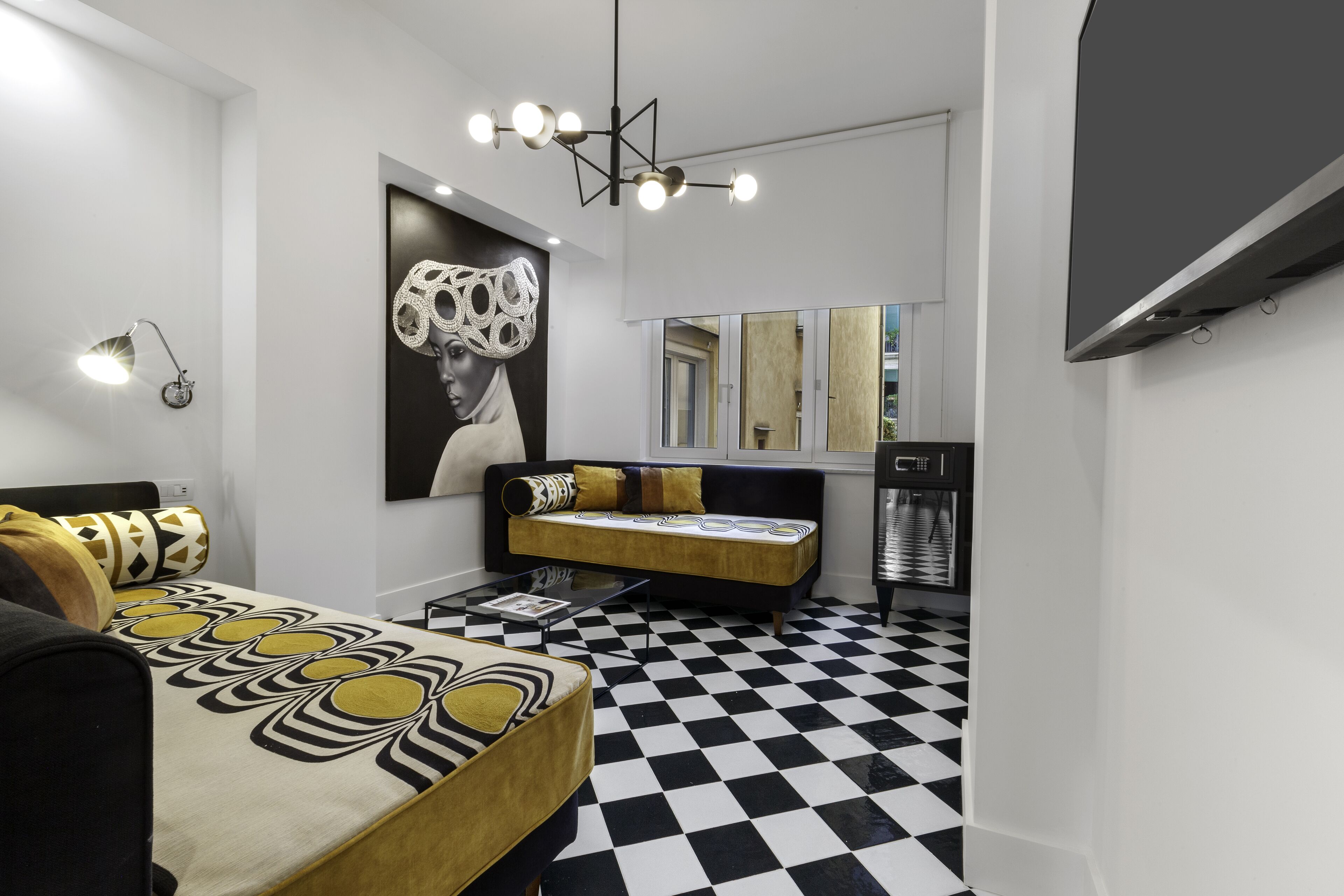 Ein modernes Schlafzimmer mit einem schwarz-weißen Schachbrettfußboden, einer Couch mit gemusterten Kissen, einem großen Spiegel und einer Deckenleuchte.