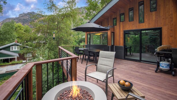 Eine Holzterrasse mit Sitzgelegenheiten im Freien, einem Feuerkorb und Blick auf einen Berg.