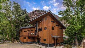 Eine moderne Holzhütte mit Balkon, umgeben von Bäumen und einem Berg im Hintergrund.