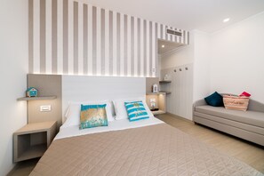 A modern hotel room with a large bed, bedside tables, a sofa, and a striped headboard. - Hotel Ariane (Rimini)