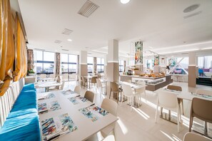 A modern dining area with a long communal table, individual dining tables, and a bar area. - Hotel Ariane (Rimini)