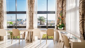Uma área de jantar moderna com uma mesa comprida, quatro cadeiras e vista para uma cidade costeira através de grandes janelas.