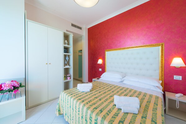 A hotel room with a large bed, a wardrobe, and a nightstand with a lamp. - Hotel Ariane (Rimini)