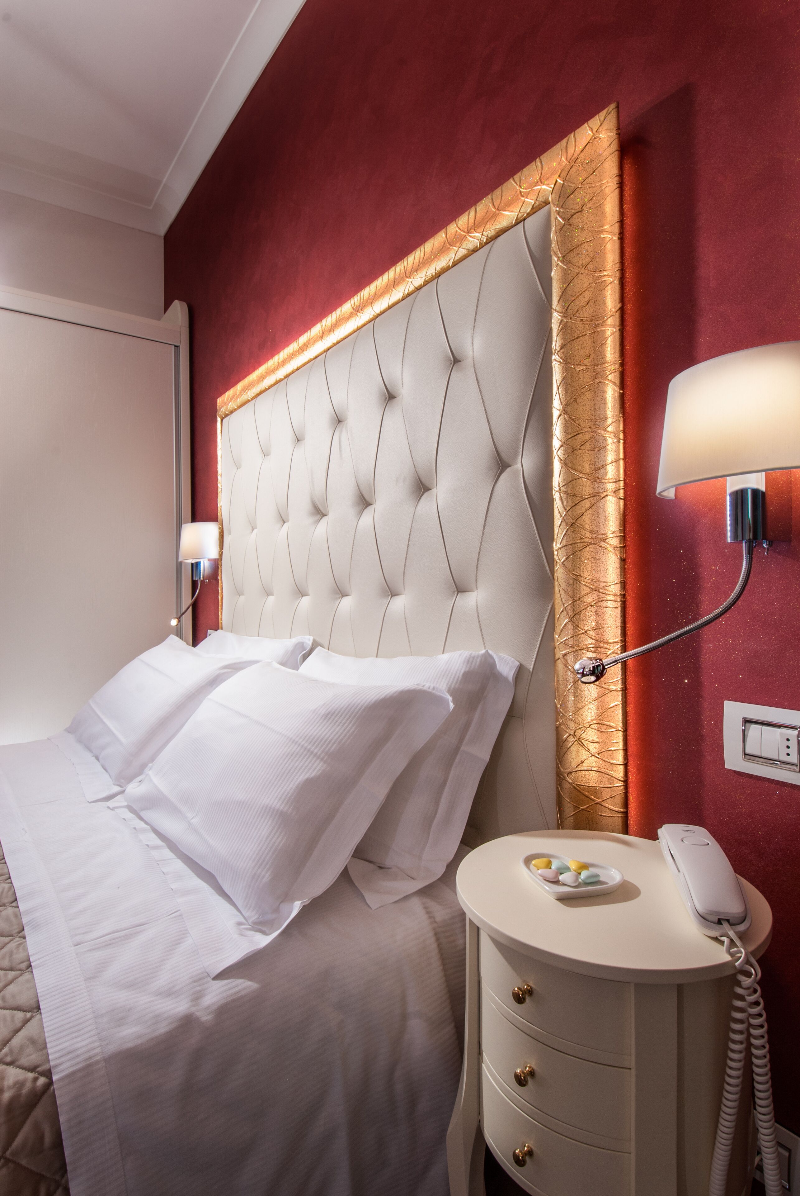 A hotel room with a tufted headboard, a bedside table with a lamp, and a telephone.