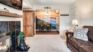 A living room with a fireplace, a brown leather sofa, a dining area with a table and chairs, and a mural on the wall.